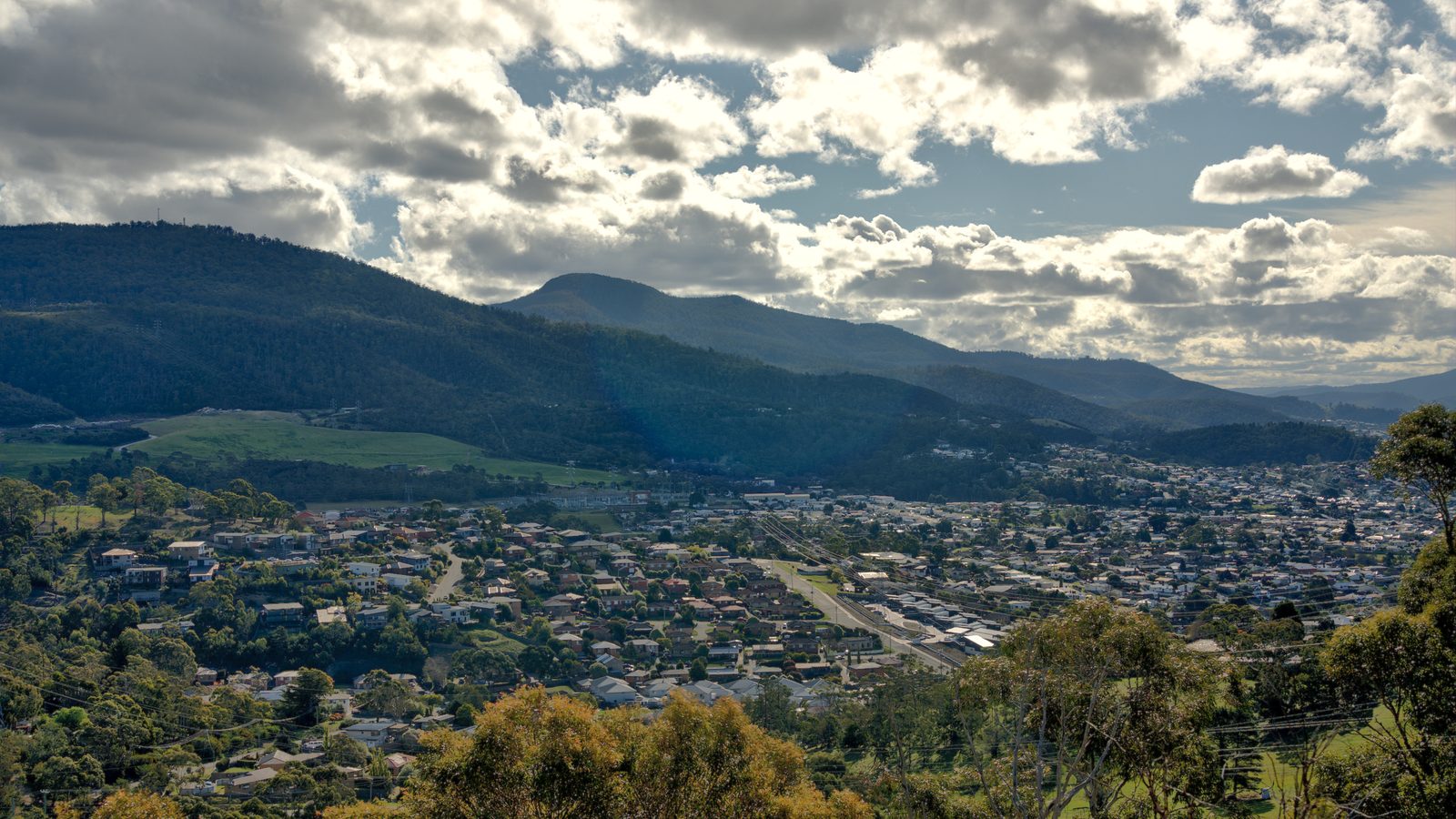 Looking across Lenah Valley rooftops and bushland to the hills beyond, under a broken sky.